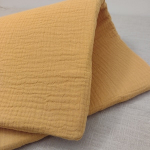 May include: A close-up of a folded piece of mustard yellow fabric with a textured surface. The fabric is soft and has a crinkled look.