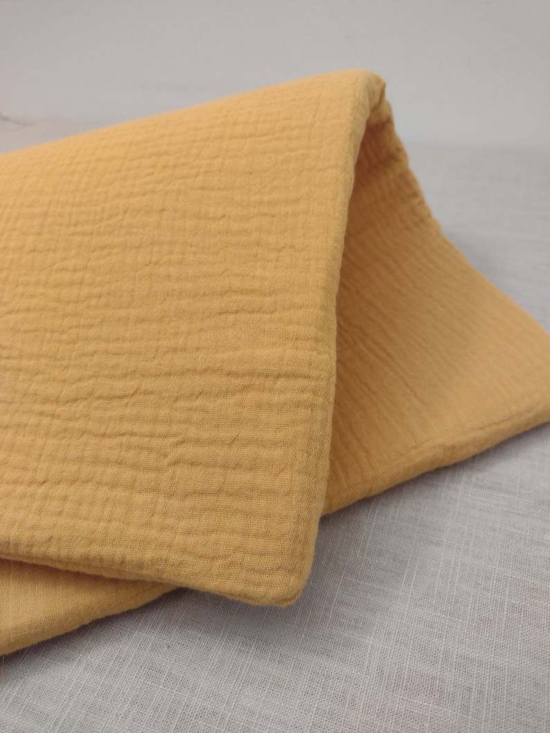 May include: A close-up of a folded piece of mustard yellow fabric with a textured surface. The fabric is soft and has a crinkled look.