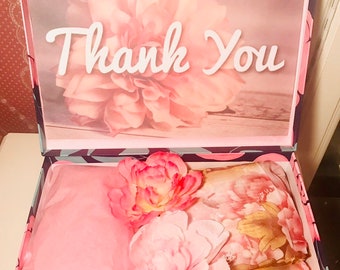 Może przedstawiać: Otwarty karton prezentowy z kwiatowym wzorem i napisem "Thank You". Pudełko zawiera różową bibułę, sztuczne kwiaty i szalik we wzory kwiatowe. Pudełko ma niebiesko-różowy wzór kwiatowy.