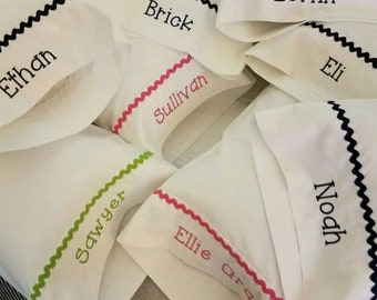 May include: White pillowcases with embroidered names in various colors. Each pillowcase has a decorative, wavy trim in black, pink, or green. Names include Ethan, Brick, Loftin, Eli, Sawyer, Noah, Sullivan, and Ellie Grace.