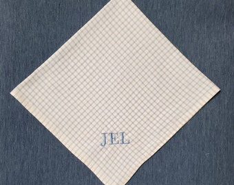 May include: White handkerchief with a light blue grid pattern and embroidered "JEL" initials. The handkerchief is square and folded diagonally, set against a blue background.