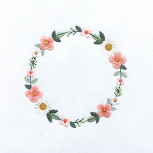 May include: A wreath of pink and white flowers embroidered on a white fabric background.