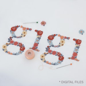 May include: The name "Gigi" embroidered with colorful flowers in red, orange, yellow, and blue. A spool of thread, pins, and loose flower embellishments are scattered around the name on a white background. The text "* DIGITAL FILES" is at the bottom.