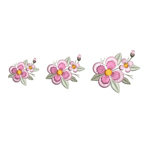 May include: Three embroidered floral designs of varying sizes. Each features pink petals, yellow centres, green leaves, and small buds. The designs are set against a plain white background, showcasing the detailed stitching.