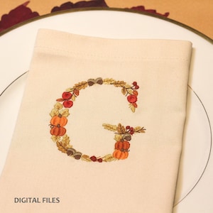 May include: A cream-colored napkin embroidered with the letter "G" in a fall-themed design. The embroidery features pumpkins, leaves, acorns, and berries in shades of orange, brown, and red. The text "DIGITAL FILES" is at the bottom.