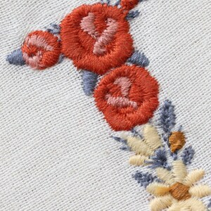 May include: Close-up of embroidered flowers in shades of orange, pink, and yellow on a white fabric background. The flowers are arranged in a vertical line, with the largest flower at the top and the smallest flower at the bottom.