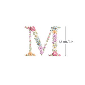 Pode incluir: Letra M bordada feita de flores coloridas, incluindo rosas, azuis e amarelas. A letra tem 7,5 cm de altura.