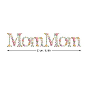 Może przedstawiać: Słowo "Mama" jest wyszyte kwiatami w kolorze różowym, żółtym i niebieskim. Haft ma 23 cm szerokości.
