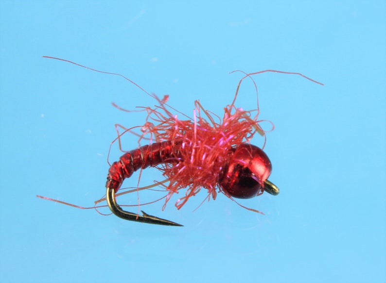 Puede incluir: Un se&ntilde;uelo de pesca con mosca rojo con cabeza de cuentas y cuerpo peludo.