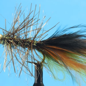 May include: A brown and black fly fishing lure with a gold bead head and a long tail of black, brown, green, and yellow feathers.