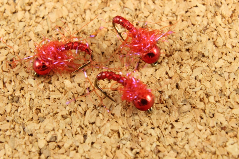 Puede incluir: Tres se&ntilde;uelos de pesca con mosca rojos con un acabado brillante y una textura peluda.