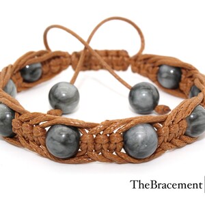 May include: A brown leather bracelet with grey gemstone beads. The bracelet is woven with a knot pattern and has a sliding closure.