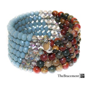 May include: A multi-strand bracelet with blue, clear, red, brown, and green beads. The bracelet is made of various materials, including glass and stone. The bracelet is wrapped around a silver charm with a wooden disc.