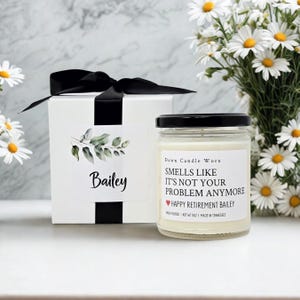 May include: A white gift box with a black ribbon and a label reading Bailey, next to a glass candle jar with a black lid. The label reads Dawn Candle Worx, SMELLS LIKE IT'S NOT YOUR PROBLEM ANYMORE, HAPPY RETIREMENT BAILEY, HAND POURED, NET WT 9OZ.