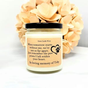 May include: A glass candle jar with a black lid and a cream-coloured wax fill. The label features the text Dawn Candle Worx and a poem about paw prints, accompanied by a heart and paw print graphic, dedicated to the memory of Toby.