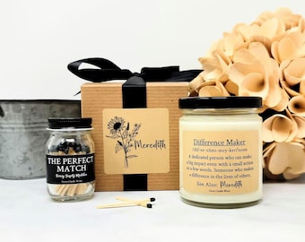 May include: A gift set with a candle, matches, and a box tied with a black ribbon. The candle jar has a black lid and a label that reads "Difference Maker." The match jar is labeled "The Perfect Match."