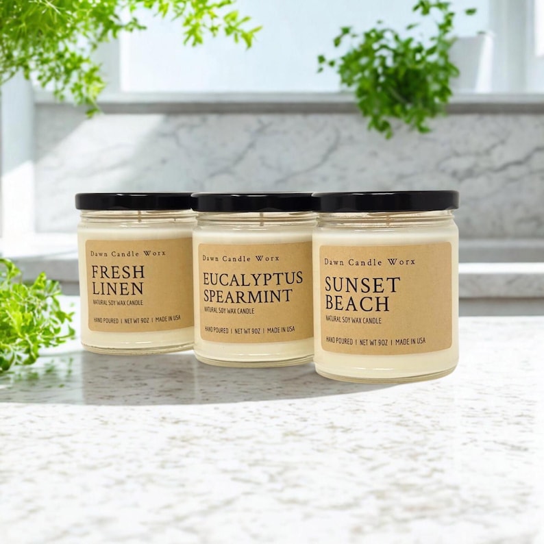 May include: Three glass jars filled with off-white soy wax, each topped with a black lid. The labels read Dawn Candle Worx, with scents labeled Fresh Linen, Eucalyptus Spearmint, and Sunset Beach, each noting a net weight of 9 ounces.