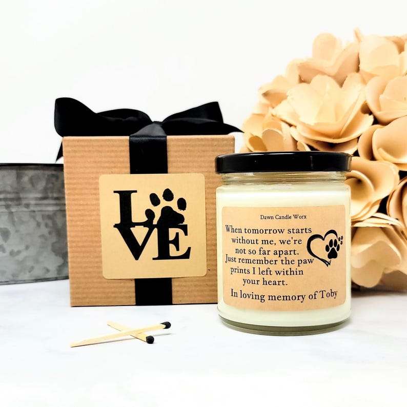 May include: A glass candle jar with a black lid and a beige label featuring the text: Dawn Candle Worx, When tomorrow starts without me, we're not so far apart. Just remember the paw prints I left within your heart. In loving memory of Toby.