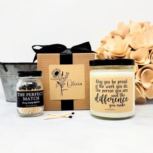 May include: A gift set featuring a candle, matches, and a decorative box. The candle has a black lid and a label with text. The match jar has a black lid and a label that reads "THE PERFECT MATCH". The box has a black ribbon.