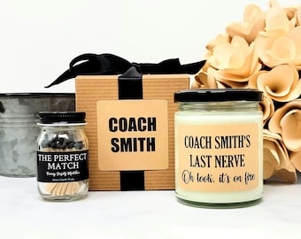 May include: A gift set featuring a candle, matches, and a decorative box. The candle has a label that reads "COACH SMITH'S LAST NERVE Oh look, it's on fire." The match jar reads "THE PERFECT MATCH Fancy Safety Matches."