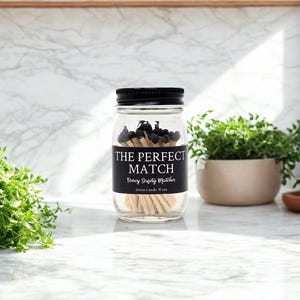 Peut inclure: Un bocal en verre transparent avec un couvercle noir rempli d'allumettes en bois. Les allumettes ont des t&ecirc;tes noires. Une &eacute;tiquette noire sur le bocal indique "THE PERFECT MATCH" et "Fancy Safety Matches".