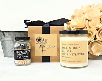May include: A gift set featuring a small glass jar of matches labeled The Perfect Match, a square cardboard box with a black ribbon and a sunflower illustration with the name Olivia, and a candle labeled Smells Like A Badass Yoga Instructor.