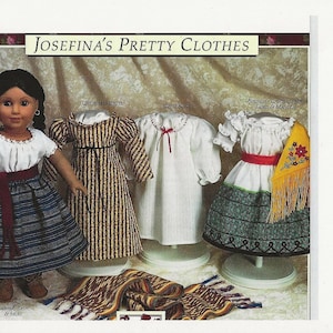 Puede incluir: Un conjunto de cuatro prendas de vestir para una muñeca llamada Josefina. El conjunto incluye una blusa blanca con una faja roja, una falda a rayas azules y blancas, un vestido a rayas marrones y amarillas, un camisón blanco y una blusa blanca con una faja roja y una falda con estampado verde y blanco. Todas las prendas de vestir para muñecas están hechas a mano y presentan detalles intrincados.