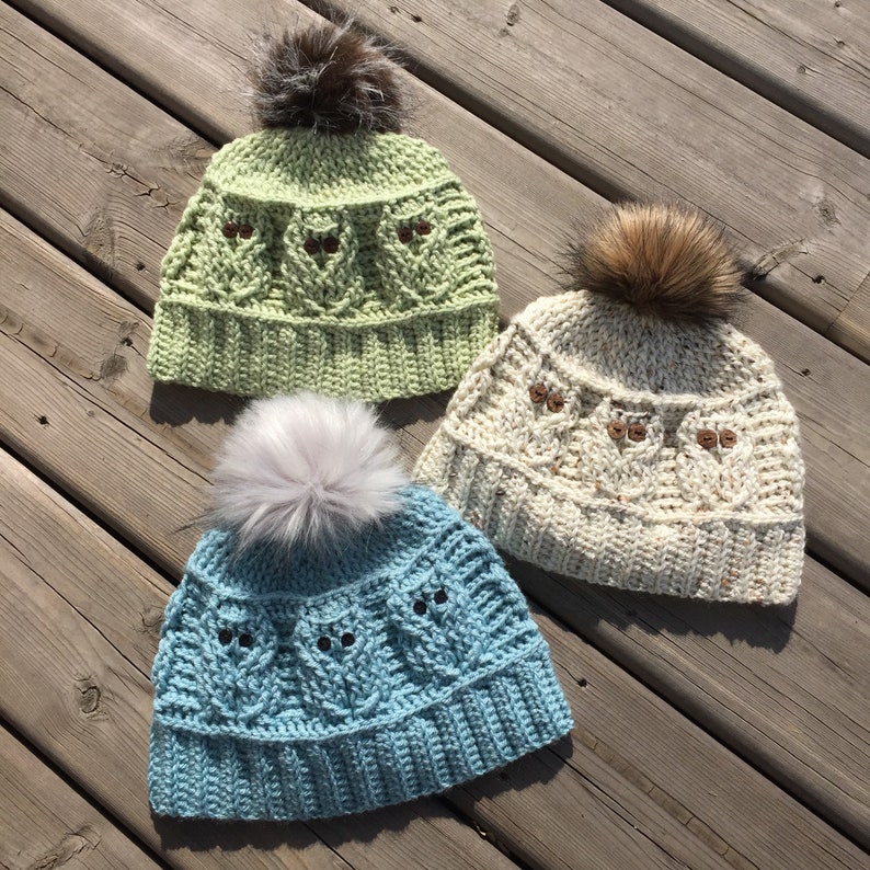 May include: Three crocheted owl hats with faux fur pom poms. The hats are in green, cream, and blue.