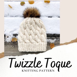 May include: A white knitted toque with a brown faux fur pom pom. The toque has a cable knit pattern and is photographed on a wooden surface with snow and leaves.