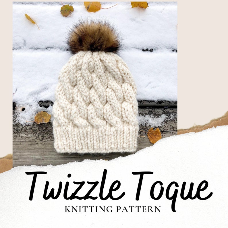 May include: A white knitted toque with a brown faux fur pom pom. The toque has a cable knit pattern and is photographed on a wooden surface with snow and leaves.