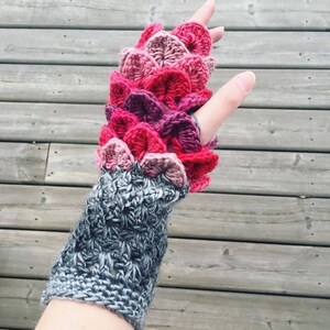 May include: A pair of fingerless gloves with a gray crocheted cuff and a pink, red, and purple crocheted dragon scale design.