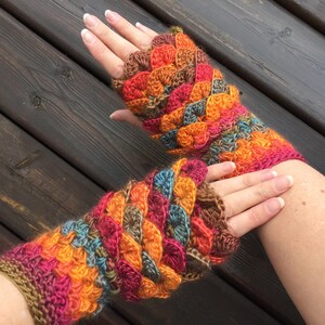 May include: A pair of colorful crocheted fingerless gloves with a textured, scaly pattern. The gloves are made with a variety of shades of orange, red, brown, and teal yarn.