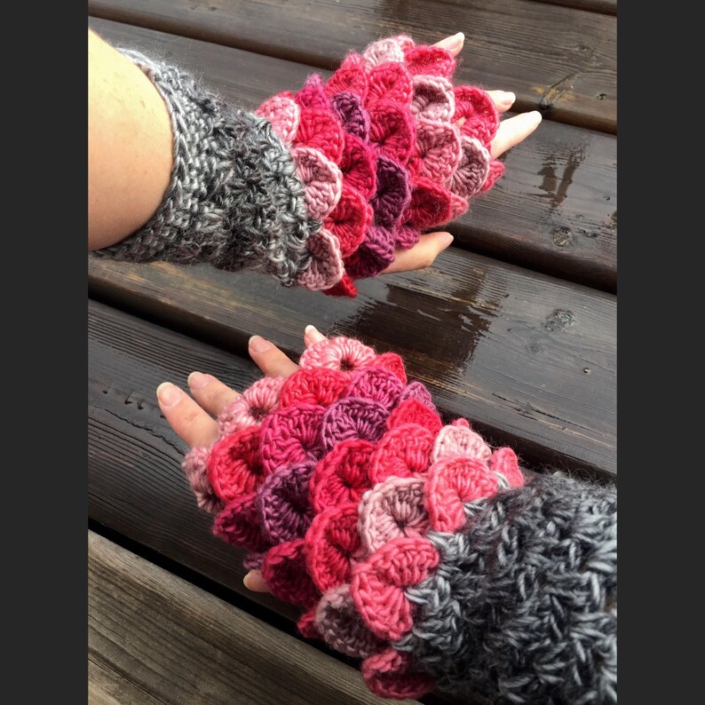 May include: A pair of pink and red crocheted fingerless gloves with a gray crocheted cuff. The gloves have a scale-like pattern.