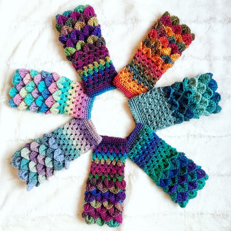 May include: Seven colorful crocheted fingerless gloves with a scale pattern. The gloves are arranged in a circle with the tips of the fingers pointing towards the center.