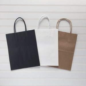 May include: Three paper gift bags in different colours: black, white, and brown. The bags have handles and are made of a sturdy paper.