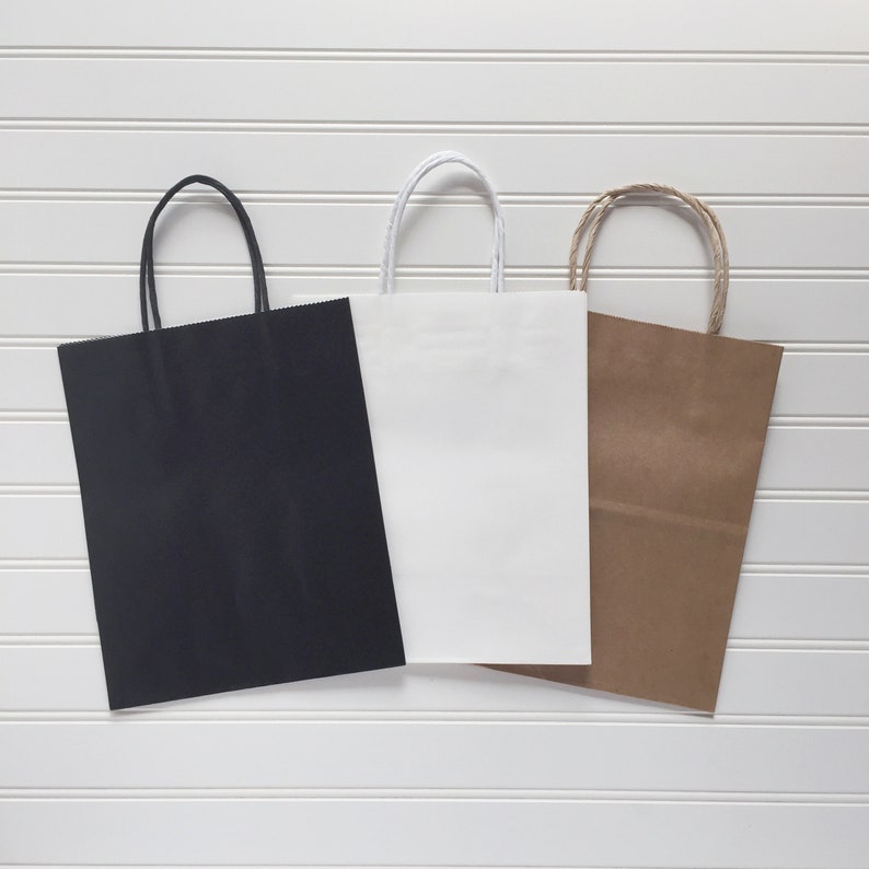 May include: Three paper gift bags in different colours: black, white, and brown. The bags have handles and are made of a sturdy paper.