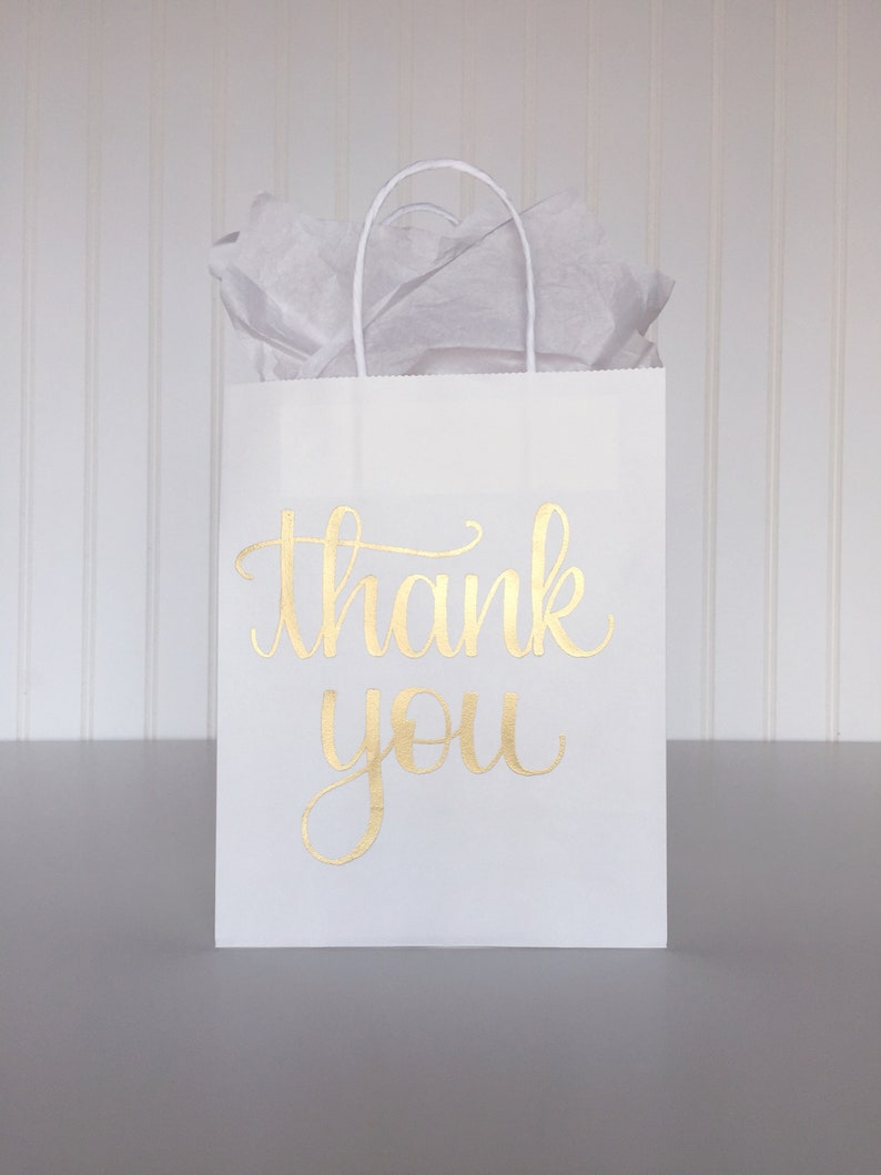 May include: White paper gift bag with gold foil lettering that says "thank you".
