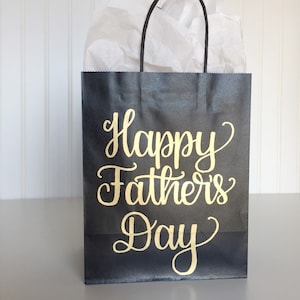 May include: Black gift bag with a gold inscription that reads "Happy Father's Day".