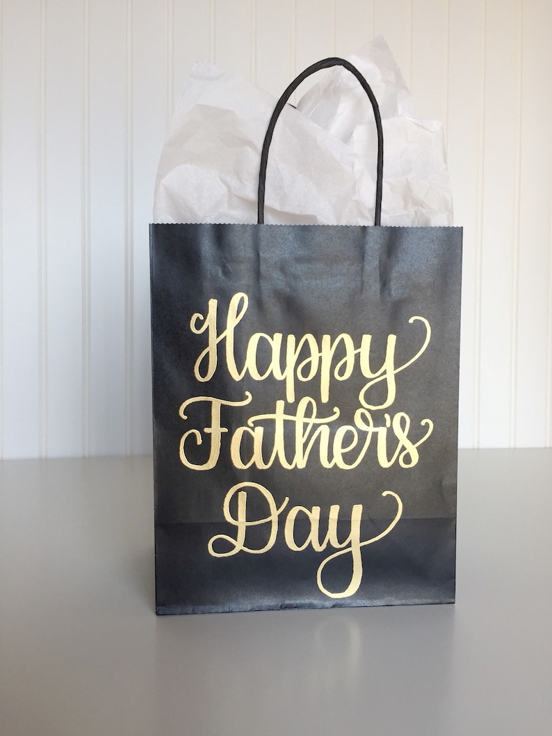 May include: Black gift bag with a gold inscription that reads "Happy Father's Day".