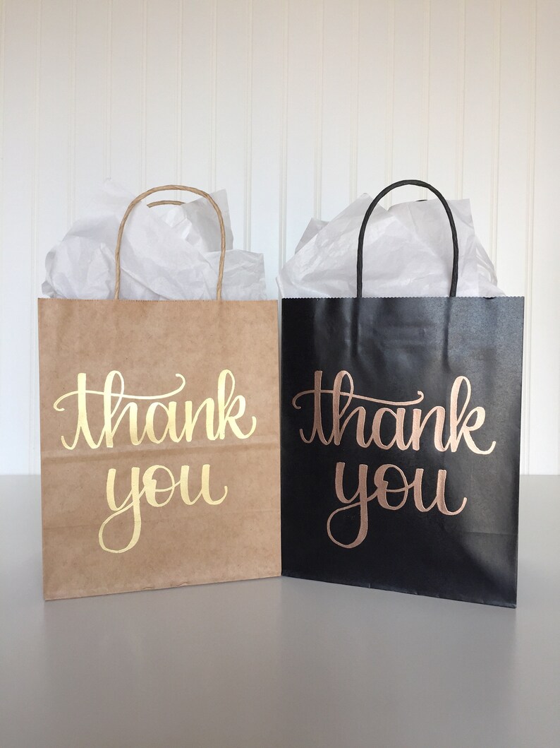 May include: Two gift bags, one brown and one black, with the words "thank you" written in gold and rose gold lettering.