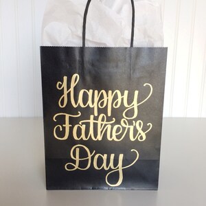 May include: Black paper gift bag with gold lettering that reads "Happy Father's Day".