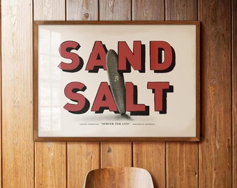 May include: A framed vintage poster with the words "SAND SALT" in red lettering. The poster features a surfboard with the text "SURFER FOR LIFE" below it.
