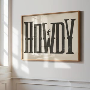 K&ouml;nnte beinhalten: Ein gerahmter Druck mit dem Wort "HOWDY" in gro&szlig;en, fetten, schwarzen Buchstaben. Eine Silhouette eines Cowboys steht auf dem Buchstaben "W".