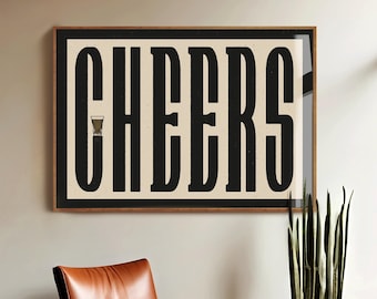 May include: A framed wall art piece with the word "CHEERS" in bold, black, vintage-style lettering. The artwork features a light beige background and a small glass icon. The frame is a dark wood color. A brown leather chair and a potted plant are in the foreground.