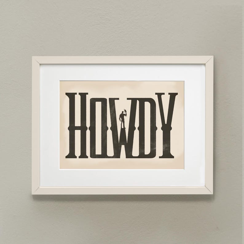K&ouml;nnte beinhalten: Ein wei&szlig;er gerahmter Druck mit beigefarbenem Hintergrund, der das Wort "HOWDY" in schwarzen, stilisierten Buchstaben zeigt. Eine kleine Silhouette eines Cowboys steht in der Mitte des Wortes.