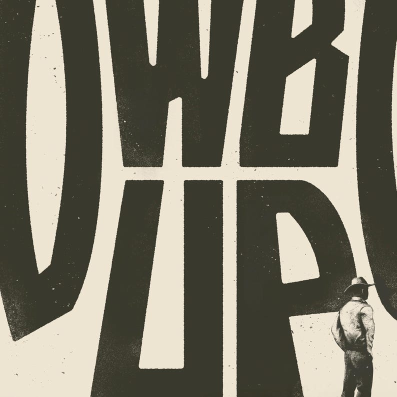 May include: Black and white graphic design with the text "COWBOY UP" in bold, block letters. A person wearing a cowboy hat and a long-sleeved shirt stands in front of the text.