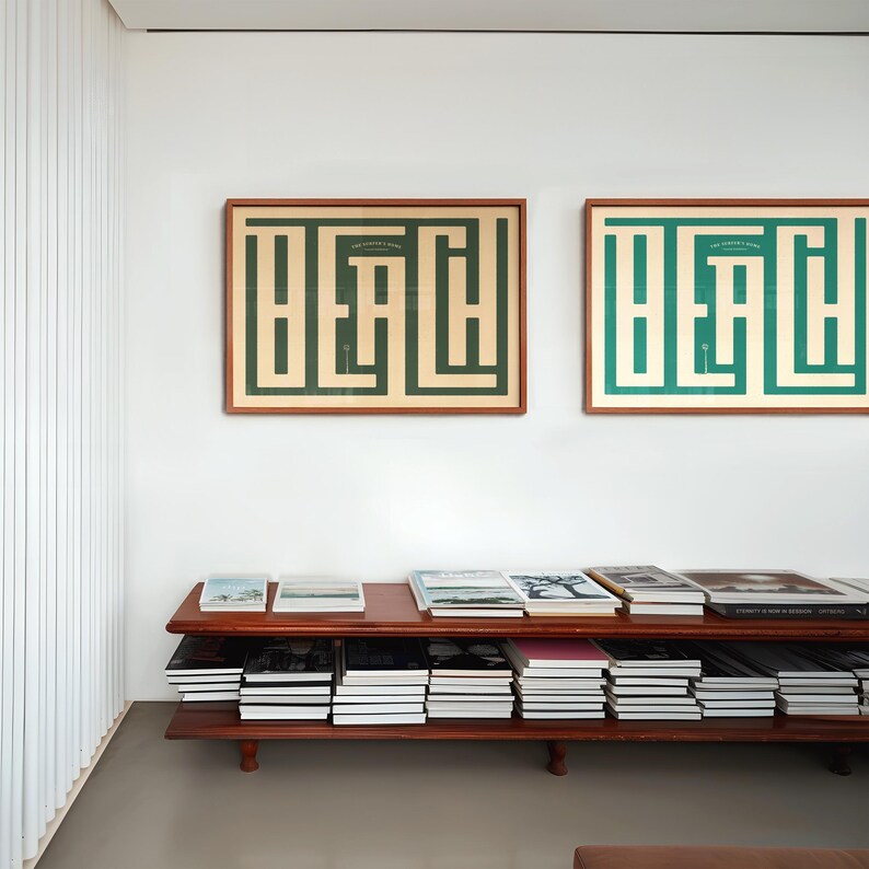May include: Two framed prints of the word "Beach" in a maze design. One print is green on a cream background, the other is brown on a cream background. The prints are hanging on a white wall above a wooden bookshelf filled with books.