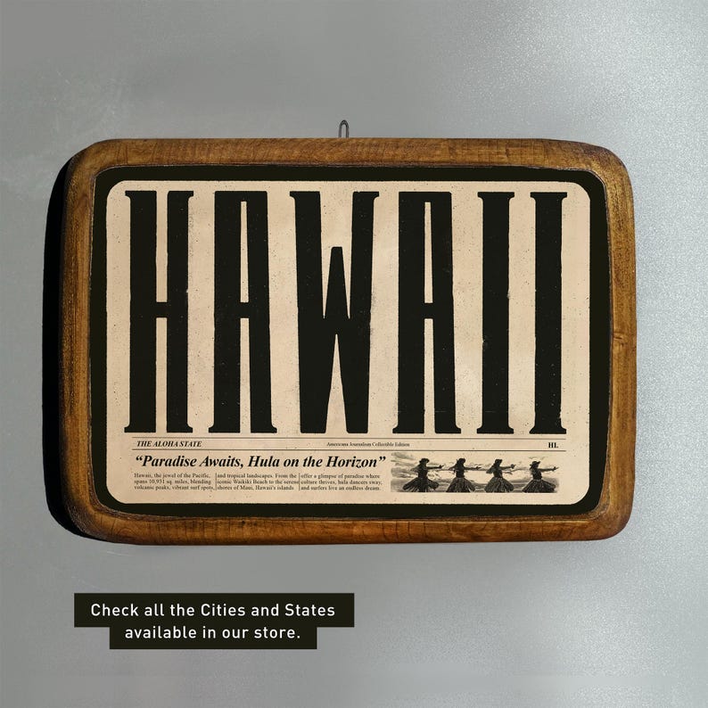 Op de afbeelding: Een houten bord met een bruin frame en een witte achtergrond. Het woord "HAWAII" is gedrukt in grote zwarte letters. De tekst "THE ALOHA STATE" is gedrukt in kleinere zwarte letters onder het woord "HAWAII". De tekst "Paradise Awaits, Hula on the Horizon" is gedrukt in kleinere zwarte letters onder de tekst "THE ALOHA STATE".