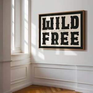 May include: A framed print with the words "WILD AND FREE" in bold black letters on a cream background.