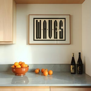 Puede incluir: Una impresi&oacute;n en blanco y negro enmarcada con la palabra "WAVES" en letras negritas y en bloque. La impresi&oacute;n est&aacute; colgada en una pared blanca sobre una encimera con un taz&oacute;n de naranjas y dos botellas de vino.